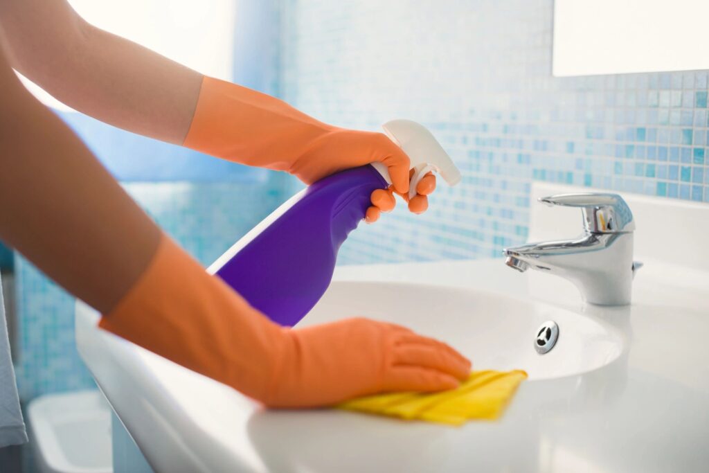 A person in orange gloves cleaning the bathroom sink.