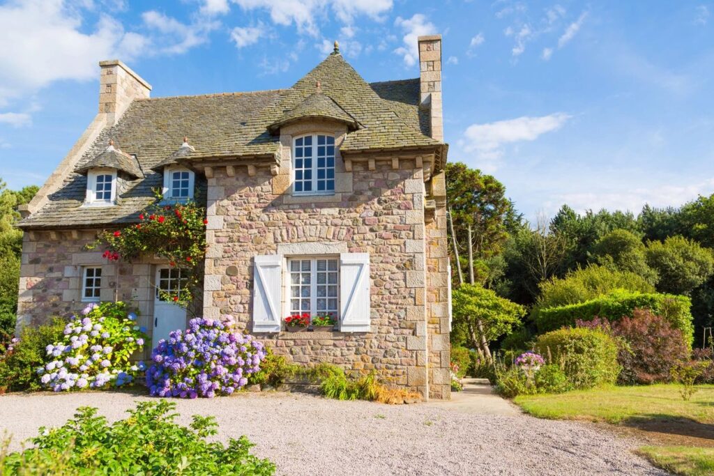 A stone house with flowers in the yard.